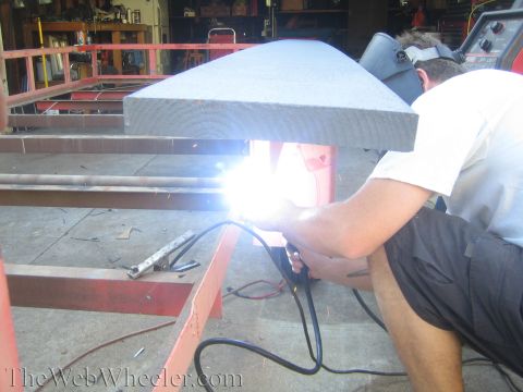 1987 Suzuki Samurai - A person welds a red metal trailer frame in a workshop, with sparks illuminating the scene.