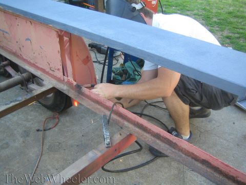 1987 Suzuki Samurai - A person welds a section of a red trailer frame, with a blue plank positioned above the work area.