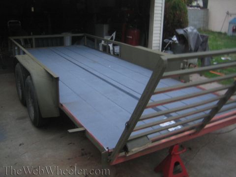 1987 Suzuki Samurai - A utility trailer with a grey deck and metal railings sits on a concrete surface.