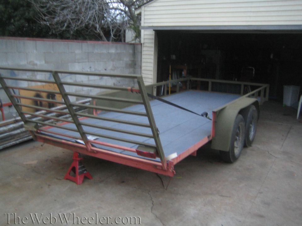 Trailer with metal railings and a grey deck, supported by a red jack