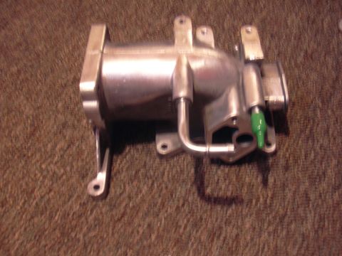 1996 Ford Crown Victoria - A metal automotive part, likely an intake manifold, rests on a textured surface. A Supermotors.net watermark is visible.