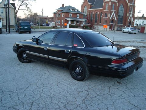 1992 Ford Crown Victoria - A black 1992 Ford Crown Victoria sedan is parked on a cracked asphalt lot with buildings in the background.