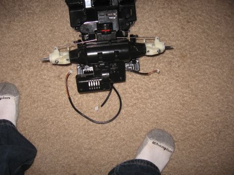 1990 Ford Bronco - A disassembled remote control car chassis sits on a carpeted floor, with feet in socks visible at the bottom.