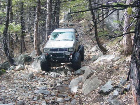 1986 Ford Bronco - This SUV is navigating a challenging, rocky terrain in a dense forest.