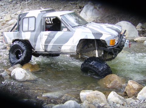 1986 Ford Bronco - This heavily modified off-road SUV navigates a challenging rocky stream bed, its extreme suspension and tire setup.