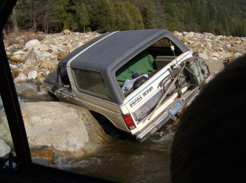 1986 Ford Bronco - This 1986 Ford Bronco appears to be stuck in a shallow riverbed, surrounded by rocks and trees.