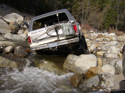 1986 Ford Bronco - This SUV is navigating a rocky stream, with a spare tire and gas can mounted on the rear.