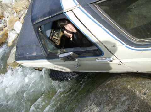 1986 Ford Bronco - A 1986 Ford Bronco navigates a rocky stream, with the driver visible through the window.