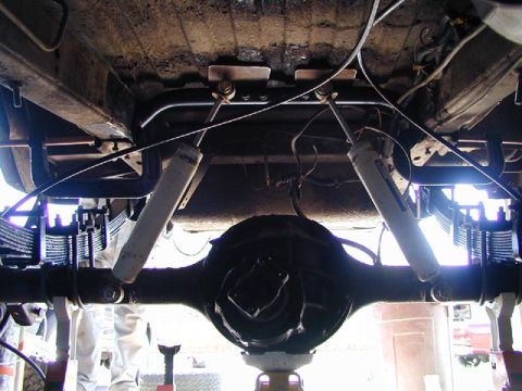 1979 Ford Bronco - The rear suspension and differential of a vehicle are visible from underneath, supported by jack stands.