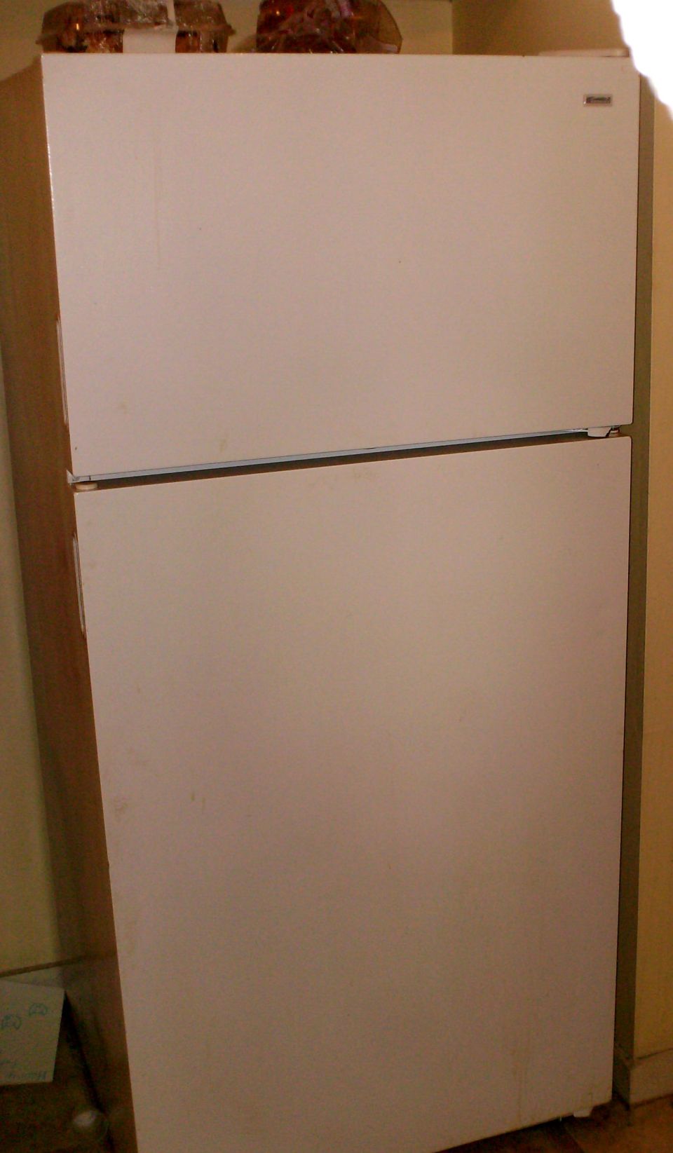 White top-freezer refrigerator against a beige wall indoors