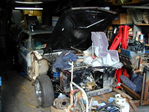 1979 Ford Bronco - Torn-down project truck in a cluttered garage with the hood raised, front fenders and grille removed and the engine bay stripped to bare ra…
