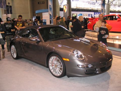 1993 Ford Taurus - A gray Porsche 911 convertible is displayed at an auto show with people around it.