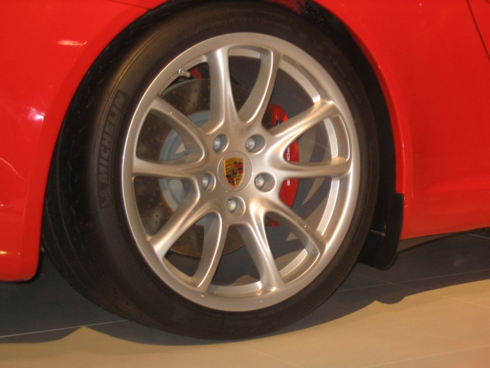 Red car wheel with silver alloy rim and Porsche crest. Red brake caliper visible