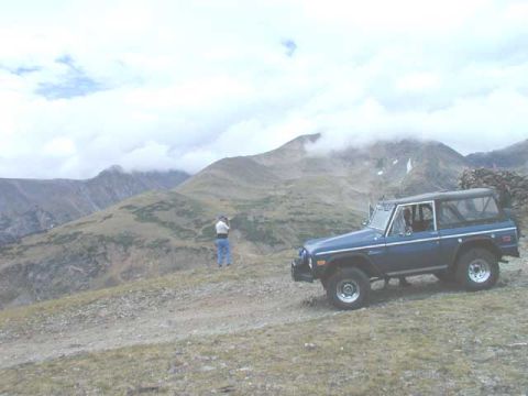 1979 Ford Bronco - A blue Ford Bronco is parked on a mountain road with a person standing nearby.