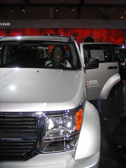 1993 Ford Taurus - A woman sits in the driver's seat of a white SUV with its door open at an auto show.