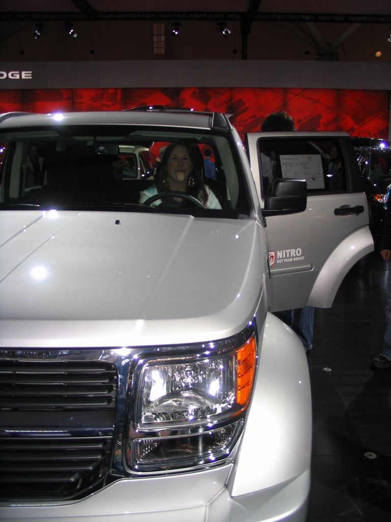White SUV with open driver's door and a woman inside, at an auto show