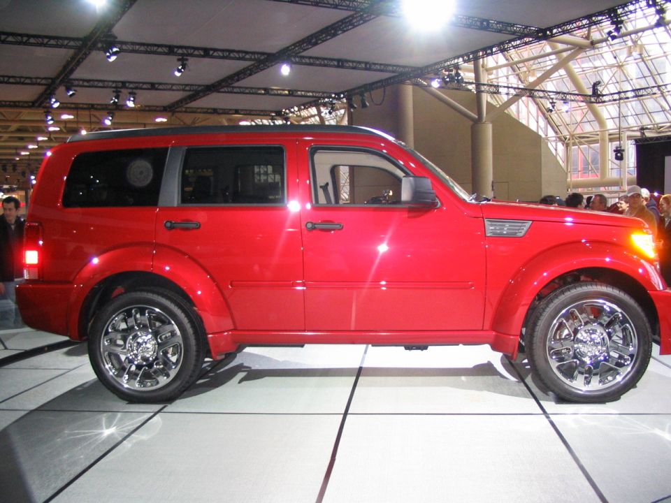 Red SUV on display indoors, side view. Chrome wheels and fender vents visible