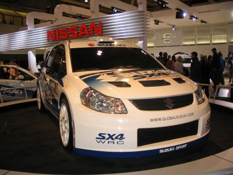 1993 Ford Taurus - Suzuki SX4 WRC rally car displayed at an auto show, "GLOBALSUZUKI.COM" and "SUZUKI SPORT" branding.