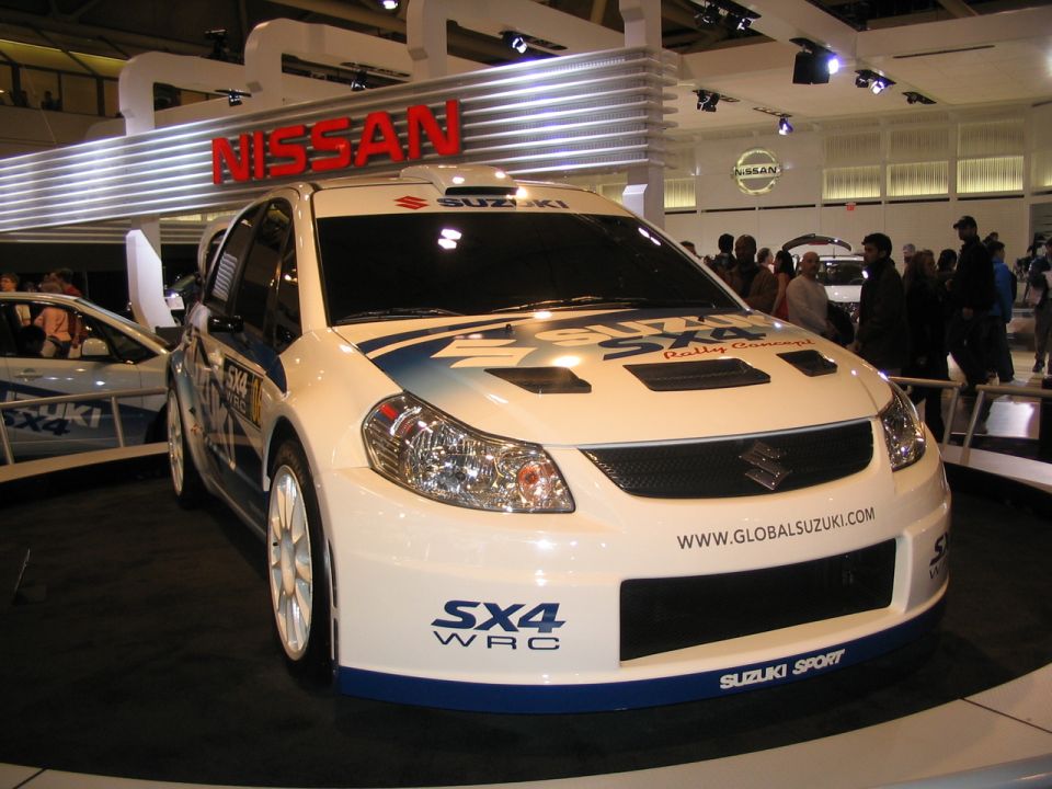 White Suzuki SX4 WRC rally car with blue graphics and "SX4 WRC" text on bumper