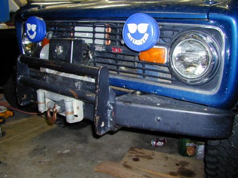 1979 Ford Bronco - The front grille and bumper of a blue 1978 Ford Bronco are visible, equipped with a winch and auxiliary lights.