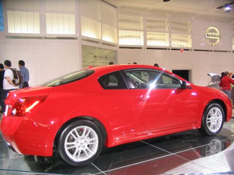 1993 Ford Taurus - A red Nissan coupe is displayed at an auto show, with people observing in the background.