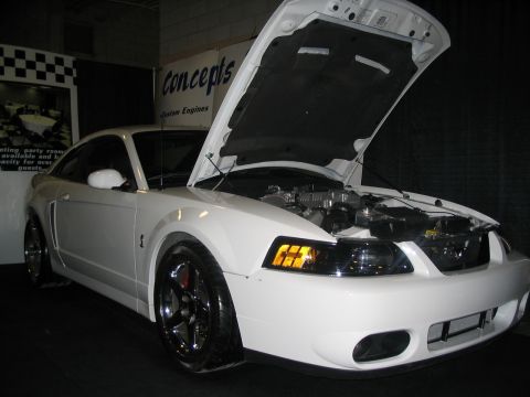1993 Ford Taurus - White Ford Mustang with its hood open, revealing the engine bay. The vehicle is displayed at an auto show.