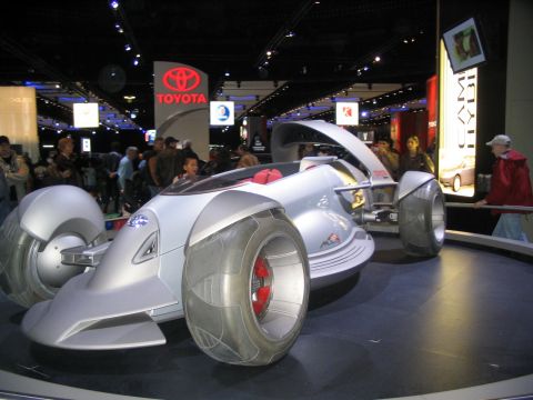 1993 Ford Taurus - A futuristic concept car is on display at an auto show, with a Toyota sign visible in the background.