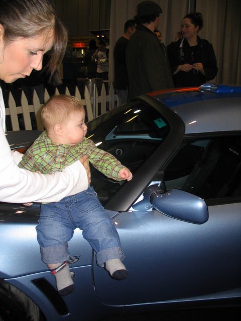 1993 Ford Taurus - Baby sits on the door of a blue car, with people in the background.