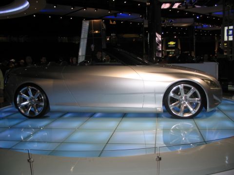 1993 Ford Taurus - A silver convertible concept car is displayed on a light-up platform at an auto show.