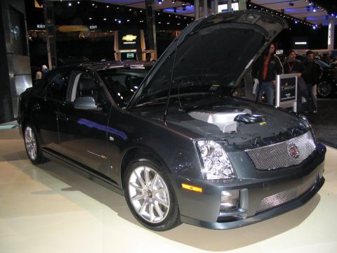 1993 Ford Taurus - This dark gray sedan, likely a Cadillac, is displayed with its hood open at an auto show.