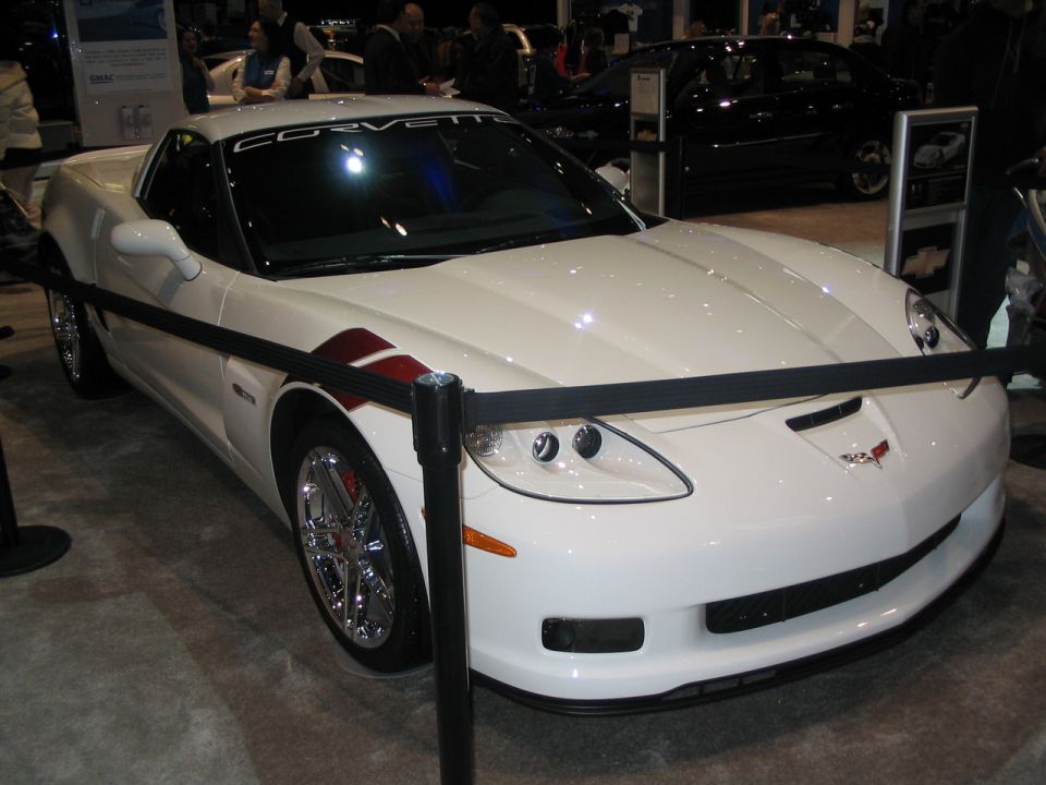White Corvette with red racing stripes on the fender, parked indoors