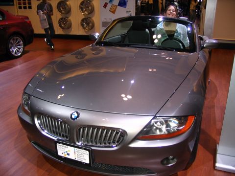1993 Ford Taurus - A woman smiles from the driver's seat of a gray BMW Z4 convertible on display at an auto show.