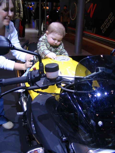 1993 Ford Taurus - A baby sits on the gas tank of a yellow and black motorcycle at an auto show.