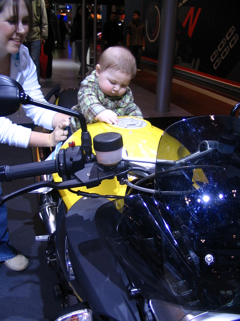 Yellow and black motorcycle with a baby sitting on the gas tank