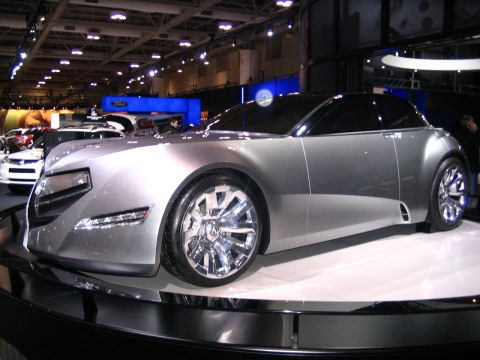 1993 Ford Taurus - A futuristic silver concept car is displayed at an auto show with other vehicles in the background.