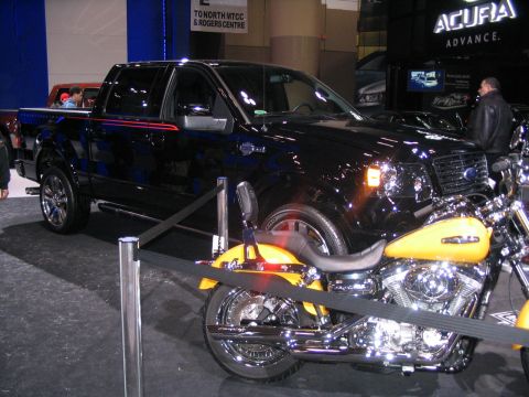 1993 Ford Taurus - A black Ford F-150 pickup truck is displayed next to a yellow motorcycle at an auto show.