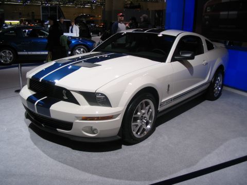 1993 Ford Taurus - A white Ford Mustang Shelby GT500 with blue racing stripes is displayed at an auto show.