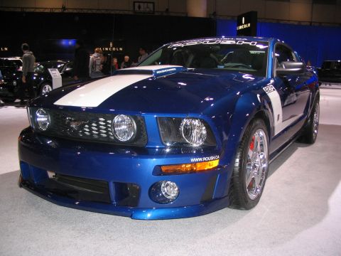 1993 Ford Taurus - A blue Ford Mustang with white racing stripes is displayed at an auto show.