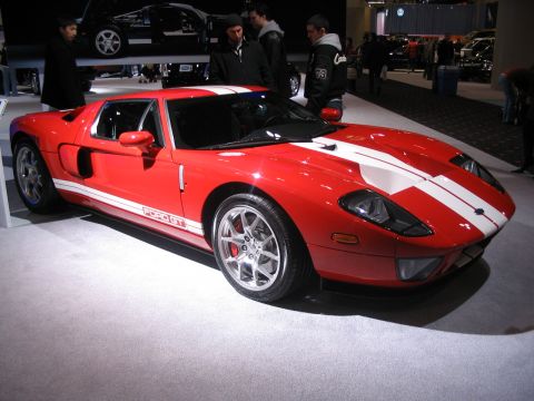 1993 Ford Taurus - Red Ford GT sports car displayed at an auto show, with other vehicles and people in the background.