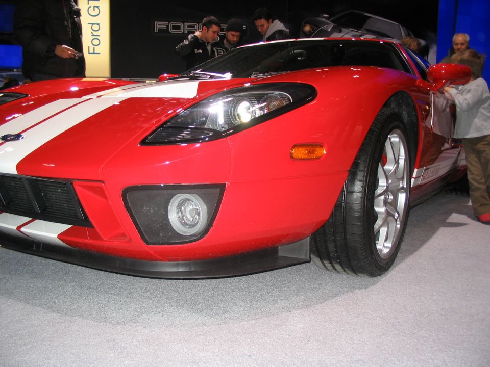 Red Ford GT sports car with white racing stripes, front quarter view, at an auto show