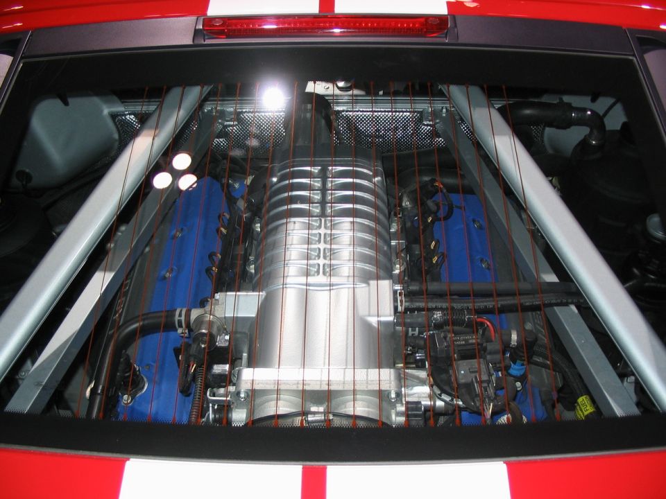 Supercharged V8 engine with blue valve covers and silver supercharger, viewed through rear window