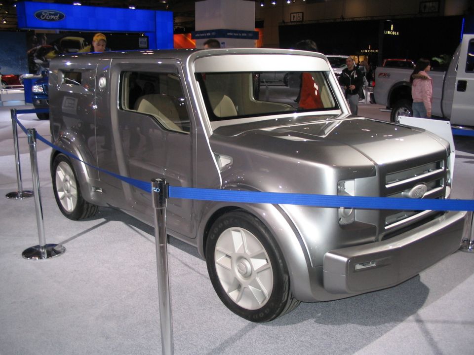 Silver concept van with a boxy rear and a Ford grille, displayed at an auto show