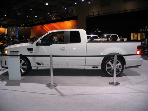 1993 Ford Taurus - A white pickup truck is displayed at an auto show with other vehicles in the background.