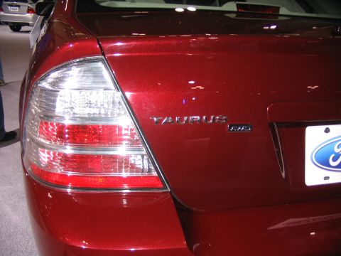 1993 Ford Taurus - Close-up of a red Ford Taurus's rear, showing the taillight and badging. Another vehicle is in the background.