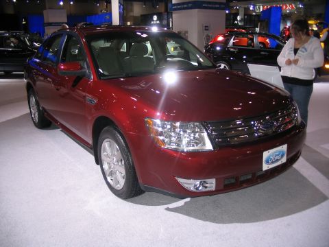 1993 Ford Taurus - A red Ford sedan is displayed at an auto show, with a "Ford" emblem on the front grille.