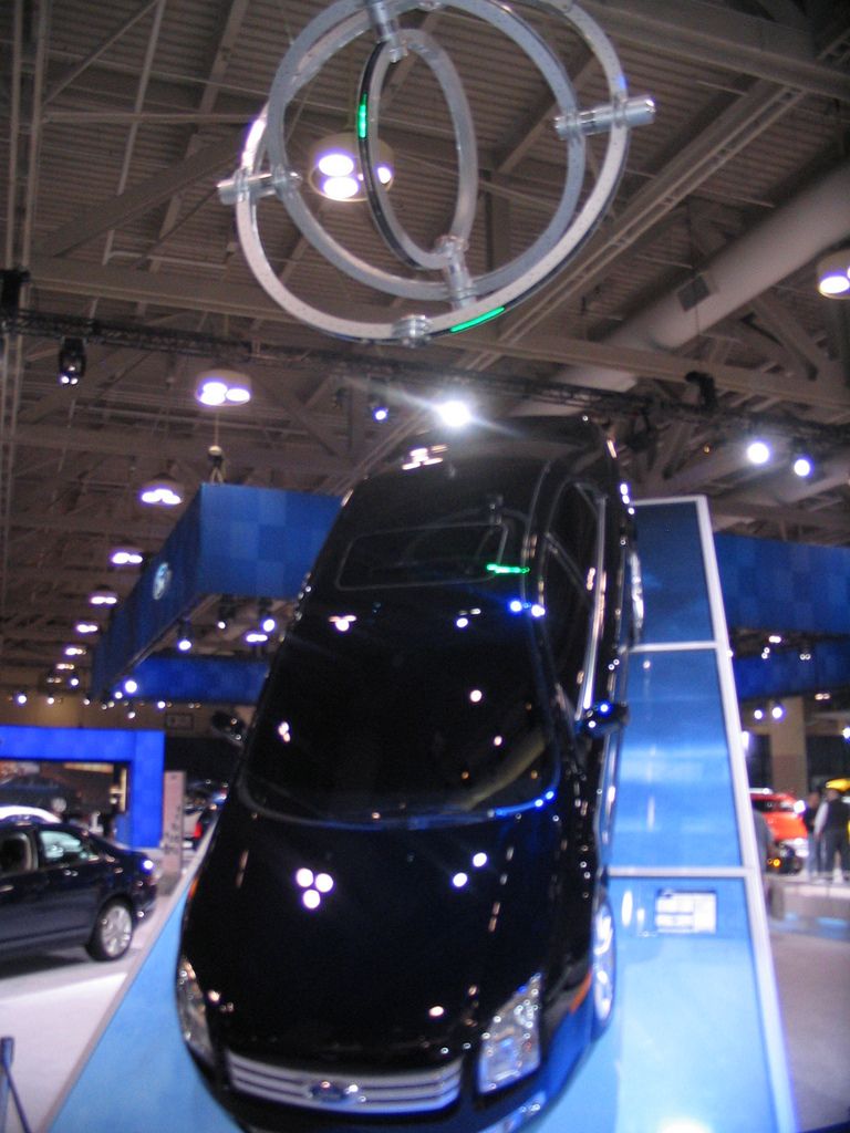 Black sedan on display ramp, with a large metal sculpture overhead