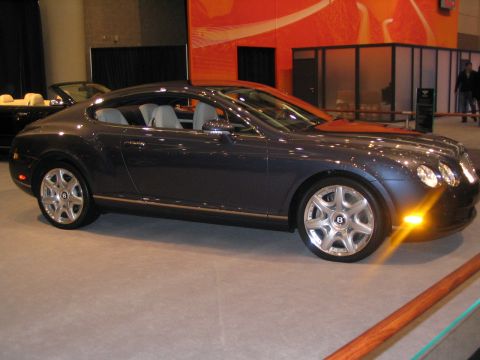 1993 Ford Taurus - A dark blue coupe with a tan interior is displayed at an auto show, with another convertible visible in the background.