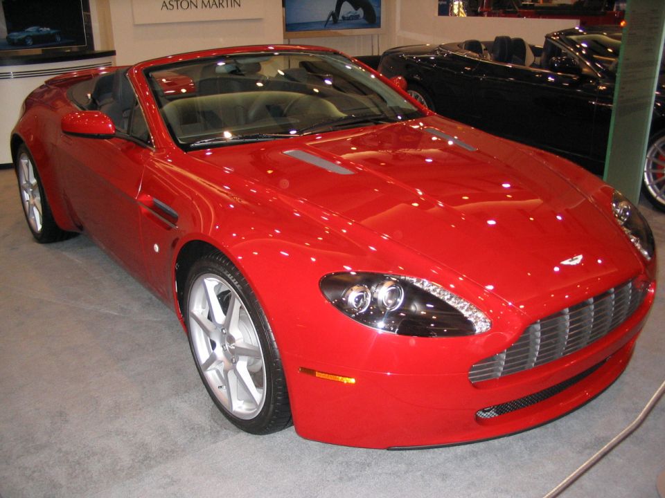 Red convertible sports car with silver wheels and a chrome grille. Black convertible in background