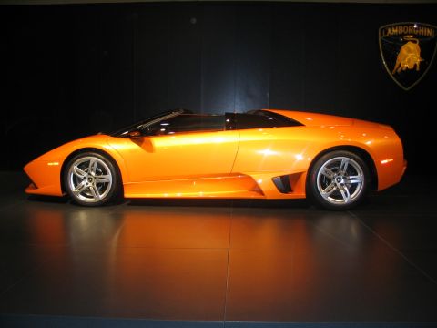 1993 Ford Taurus - Orange Lamborghini sports car displayed indoors with a black backdrop and logo.