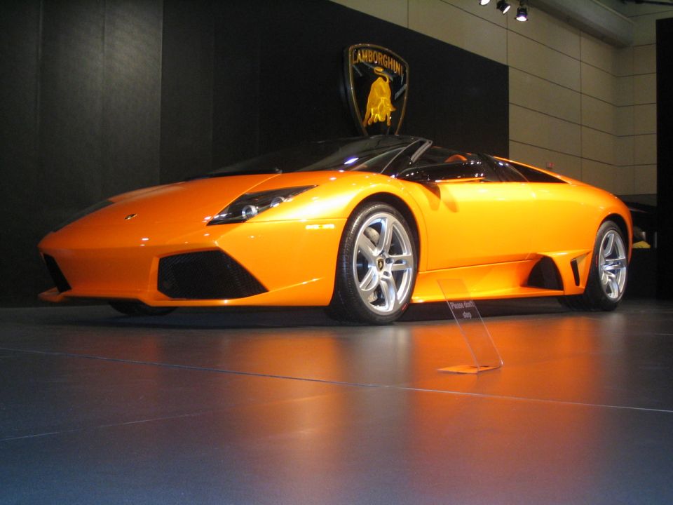 Orange Lamborghini convertible on display with Lamborghini logo behind it